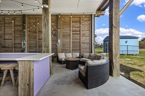 Une terrasse extérieure avec un espace bar, des sièges et une vue sur un bâtiment bleu en arrière-plan.