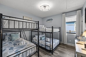 A bunk bed room with a ceiling light fixture, a framed picture on the wall, and a window with curtains. - Salty Pelican | Easy Beach Access | Fenced Yard (Bolivar Peninsula)
