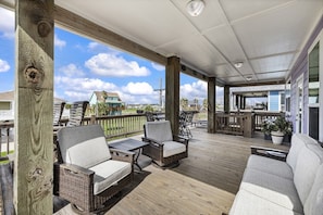 A covered outdoor deck with wicker furniture and a view of the surrounding area. - Salty Pelican | Easy Beach Access | Fenced Yard (Bolivar Peninsula)