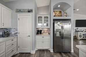 A kitchen with white cabinetry, a stainless steel refrigerator, and a coffee maker. - Salty Pelican | Easy Beach Access | Fenced Yard (Bolivar Peninsula)
