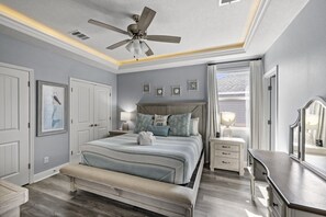 A bedroom with a bed, bedside tables, a ceiling fan, and a window with curtains. - Salty Pelican | Easy Beach Access | Fenced Yard (Bolivar Peninsula)