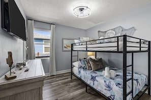 Un lit superposé avec une couvre-lit à motifs, un bureau avec un miroir et une fenêtre avec des rideaux.