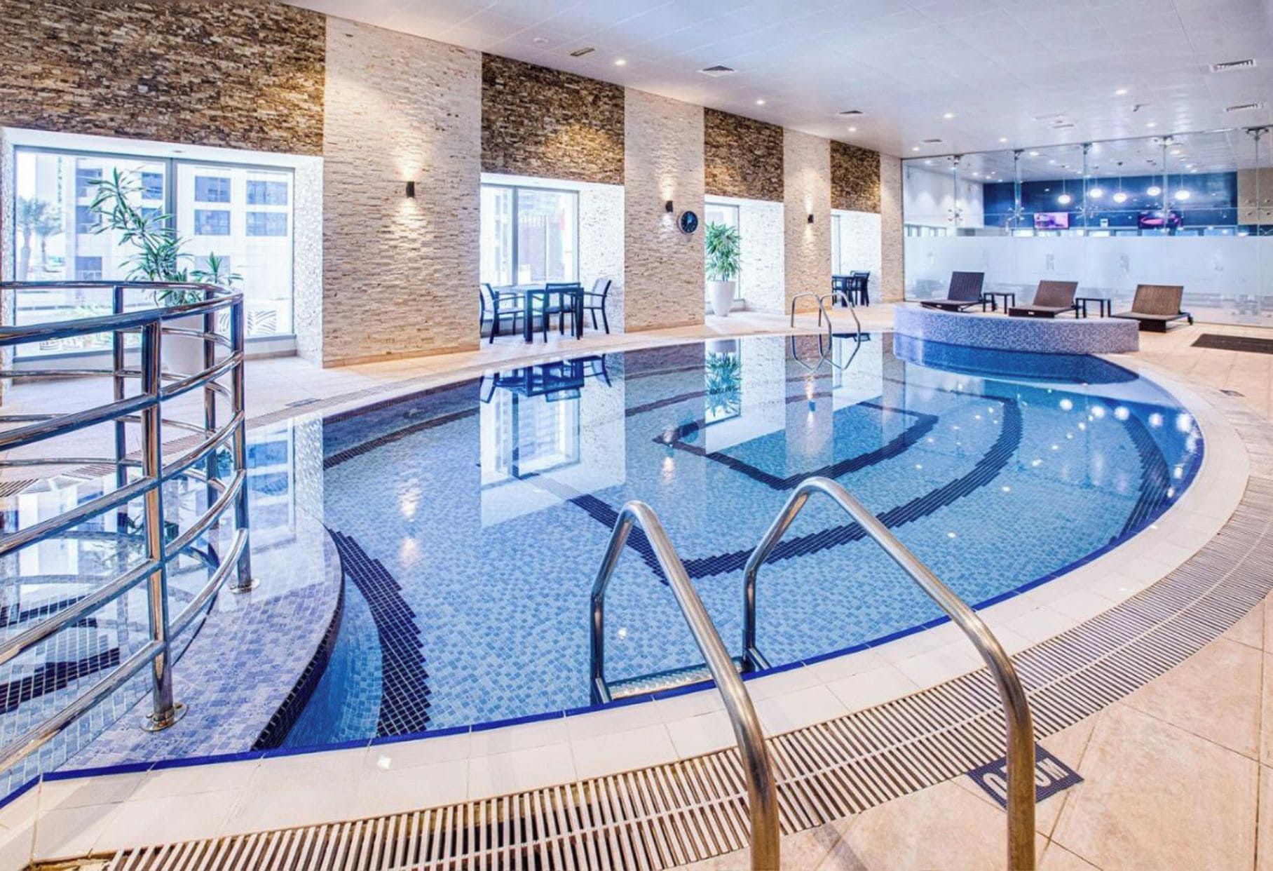 Piscina interior moderna con agua cristalina, rodeada de sillones de descanso y una zona de recepción.