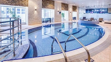 Piscina interior moderna con agua cristalina, rodeada de sillones de descanso y una zona de recepción.