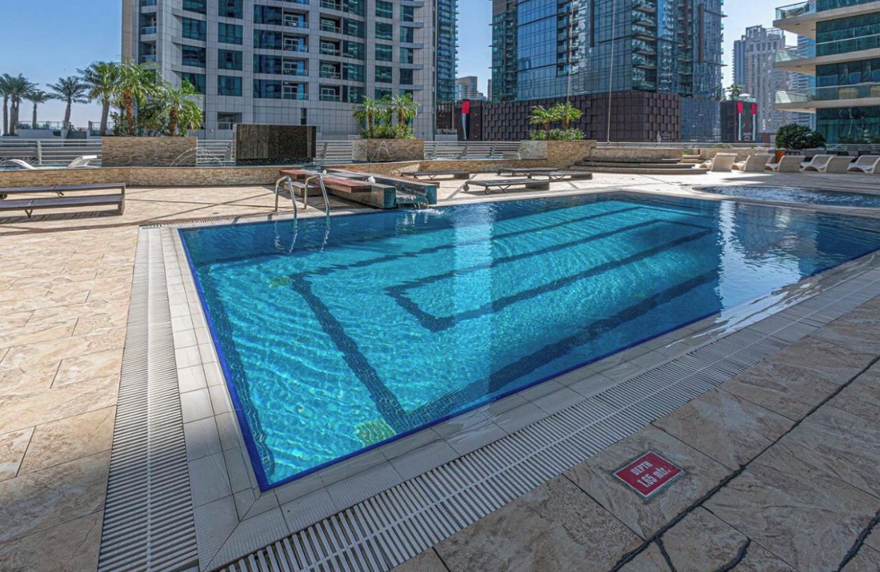 Una piscina con tabla de clavados, sillas de descanso y vistas de edificios altos.