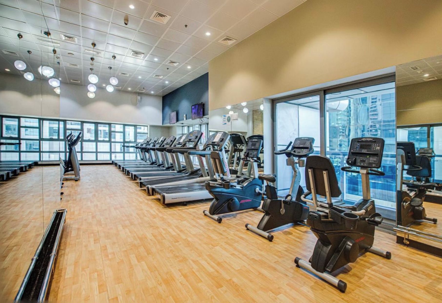 Un gimnasio con varias caminadoras, elípticas y una máquina de remo.