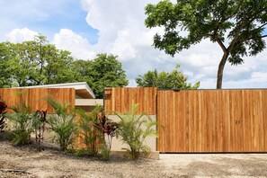 Une clôture en bois, avec un bâtiment moderne en arrière-plan, le tout entouré de différentes plantes.