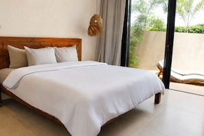 Une chambre à coucher avec un lit en bois, du linge de lit blanc, un luminaire suspendu et une vue sur un jardin, visible à travers une porte vitrée.