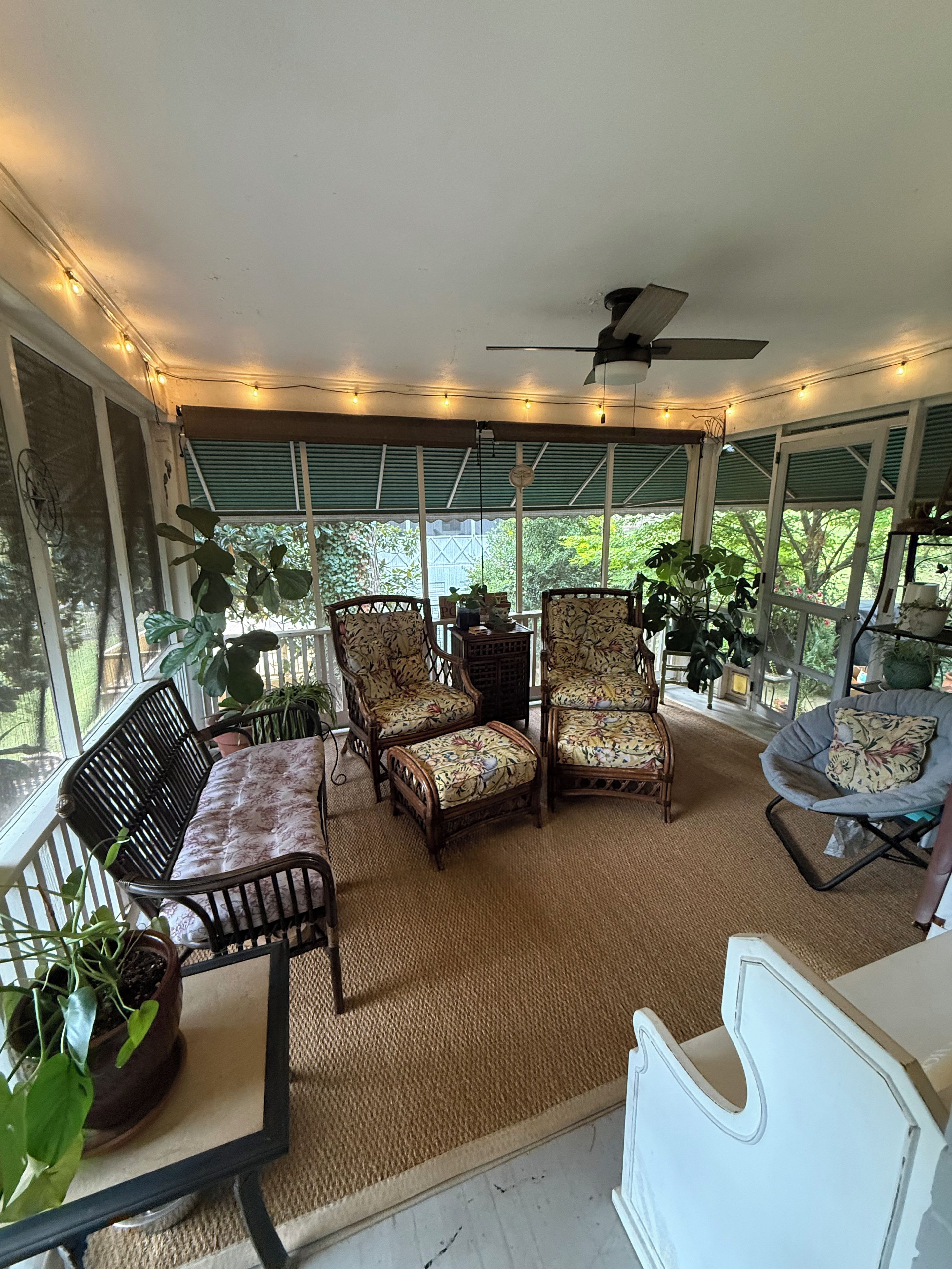 A covered patio area with seating, string lights, and potted plants.