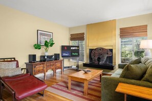 A living room with a sofa, a red chair, a wooden coffee table, a TV with streaming service logos, a fireplace with a decorative animal sculpture, and a window with a view. - Eclectic South Austin Home w Flex Studio Room & Covered Patio (Austin)