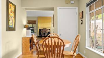 A dining area with a round table and wooden chairs, a fireplace, and a view through a window.