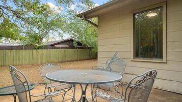 A patio with a round metal table and chairs, a wooden fence, and a house with a window.