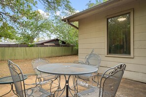 A patio with a round metal table and chairs, a wooden fence, and a house with a window. - Eclectic South Austin Home w Flex Studio Room & Covered Patio (Austin)