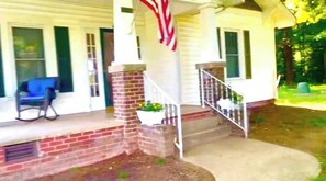 A porch with a brick column, a white railing, and a blue chair. - 3-bedroom house in charming Salisbury with cool AC (Salisbury)