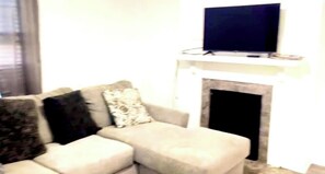 A living room with a sofa, a flat-screen TV mounted above a fireplace. - 3-bedroom house in charming Salisbury with cool AC (Salisbury)