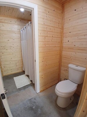 Ein kleines Badezimmer aus Holz mit Toilette, einer Duschvorhang und einem weißen Teppich.