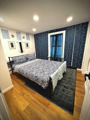 Une chambre à coucher avec un lit, une fenêtre avec des rideaux, un mur à motifs et un plancher en bois.