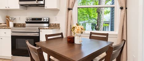 A kitchen with a microwave, oven, and stove, a dining table with chairs, and a window with curtains.