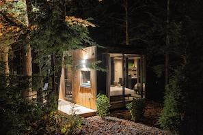 A cabin with a glass door entrance, a visible bed, and a small window. - The Moss Rock | Mirror Cabin + Spa at Uncommon Accommodations - Smuggler's Notch (Cambridge)