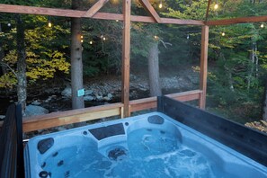 A hot tub with a wooden deck and a view of a forested area. - The Moss Rock | Mirror Cabin + Spa at Uncommon Accommodations - Smuggler's Notch (Cambridge)
