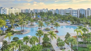 Ein Resort mit mehreren Schwimmbecken, Palmen und einem großen Gebäudekomplex im Hintergrund.