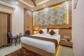 Una habitación de hotel con una cama grande, un escritorio con silla, una mesita y una obra de arte colgada en la pared.