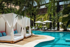 Zona junto a la piscina con una cama con dosel, sillones de descanso y sombrillas.