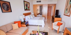 Una habitación de hotel con cama, sofá, sillón, televisión y obras de arte en las paredes.
