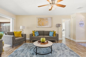 A living room with a ceiling fan, two sofas with cushions, a coffee table, and a painting on the wall. - 3-bedroom house in Seminole with lanai and temperature controlled pool. (Seminole)