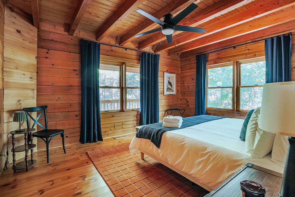 A wooden cabin bedroom with a bed, a chair, a table, and a ceiling fan.