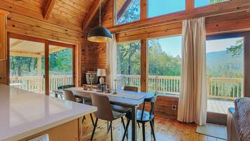 A wooden cabin interior with a dining area, large windows, and a view of the outdoors.