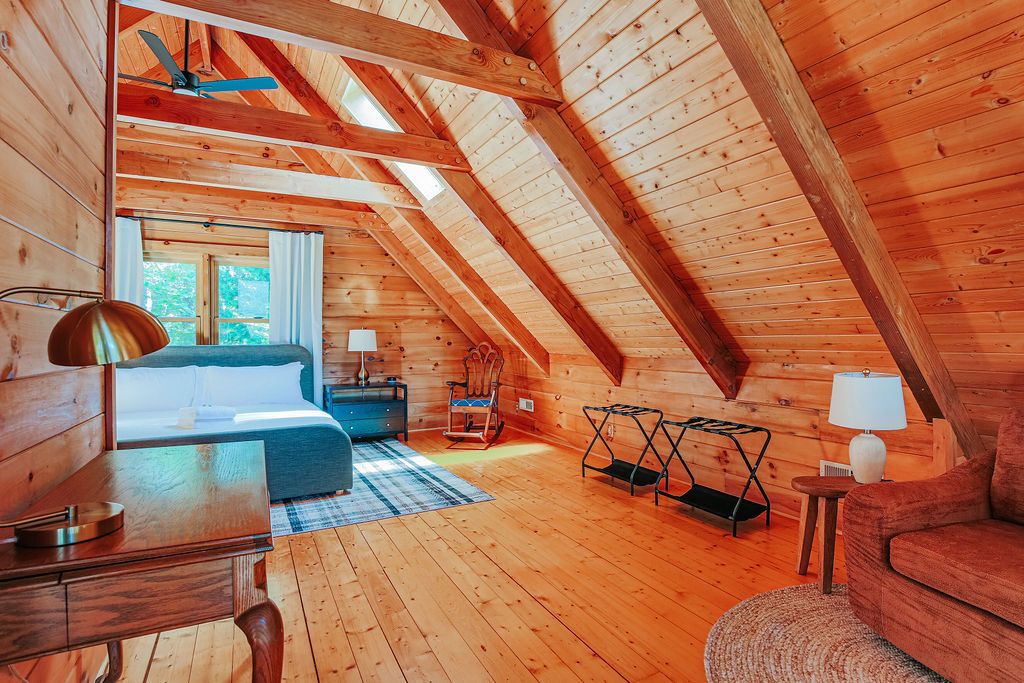 Un intérieur en bois avec un plafond en pente, un lit, un bureau, une chaise et une lampe.