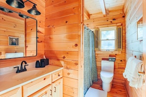 A wooden cabin bathroom with a sink, mirror, toilet, and a window with shutters. - Afton View Lodge (Afton)