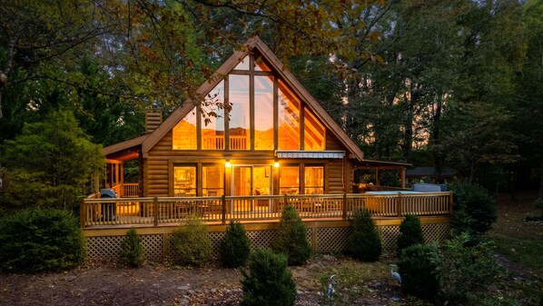 A log cabin with a large deck, surrounded by trees.