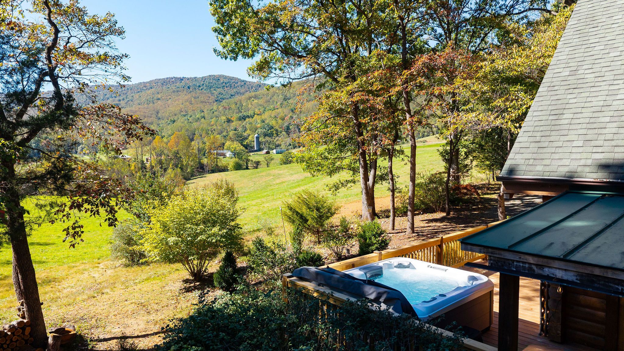 A hot tub on a wooden deck with a view of a green field and trees.