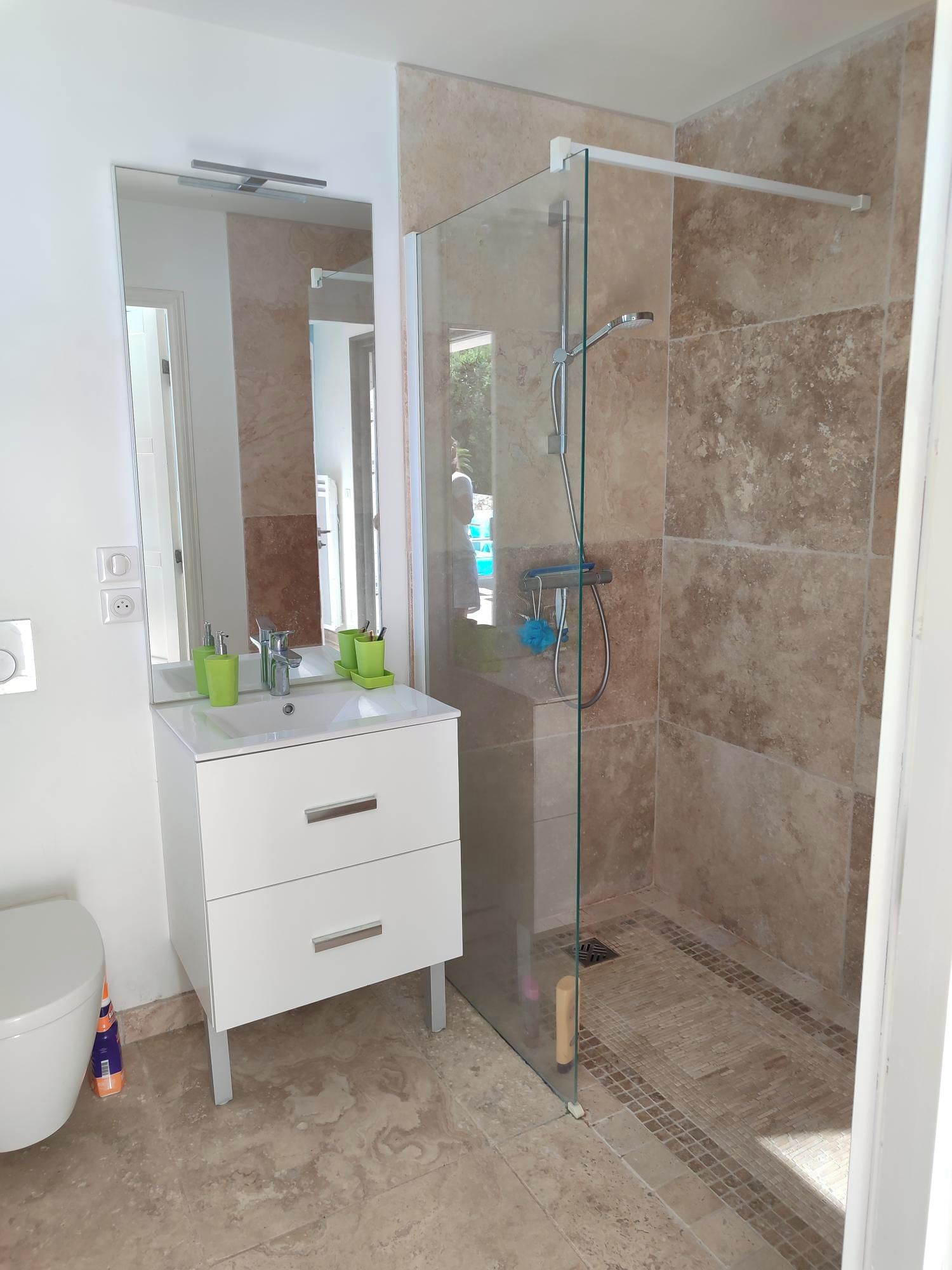 A modern bathroom with a glass shower enclosure, a white vanity with drawers, and a large mirror.