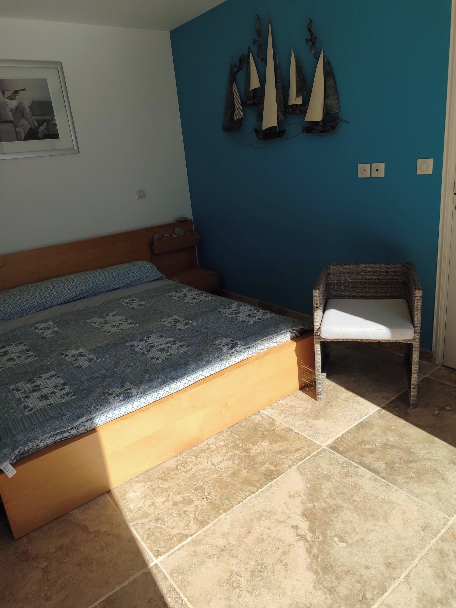 A bedroom with a bed, a chair, a wall with decorative elements, and a framed picture.