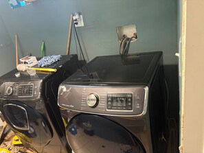 Two front-loading washing machines in a room with a green wall, a power outlet, and a visible plumbing fixture. - Midway comfortable home that sleeps 10. 5 mins to MDW; 15 mins to dwtn. (Chicago)