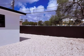Ein Gebäude mit weißer Fassade, Kiesgrundstück und einer dunklen Mauer im Hintergrund.