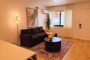Un salón con sofá, una mesa de centro, una lámpara, una planta y una ventana con cortinas.