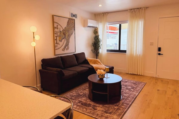 Sala de estar com sofá, mesa de centro, luminária, planta e janela com cortinas.