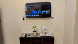 A wall-mounted TV displaying a user interface with various options. Below the TV, there is a small table with a potted plant, a coffee maker, and a tray with cups and condiments. - Tremendous 2-bedroom apartment with AC in Red Sea, Hurghada (Red Sea Governorate)