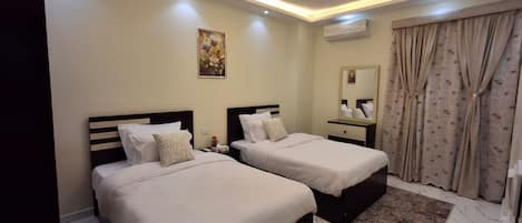 A hotel room with two beds, a nightstand, a mirror, and a window with curtains.