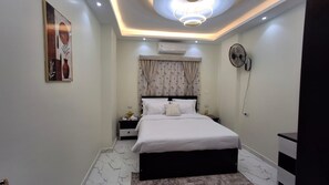 Een moderne slaapkamer met een bed, nachtkastjes, een airconditioner, een ventilator aan de muur en een plafondlamp.