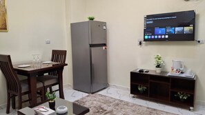 Een knus woongedeelte met een eethoek, een koelkast, een flatscreen televisie aan de muur en een klein koffiehoekje.