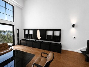 Un salon moderne doté d’une grande fenêtre, d’un meuble de rangement noir pour appareils électroniques, d’un canapé en cuir et d’une table basse en verre.
