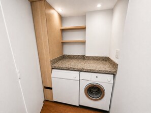 Une petite buanderie comprenant un lave-linge, un plan de travail et des meubles de rangement en bois.