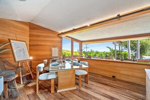 A modern dining area with a glass table, wooden chairs, and a view of greenery outside. - Casa Seraphina by Oraklus (Los Angeles)