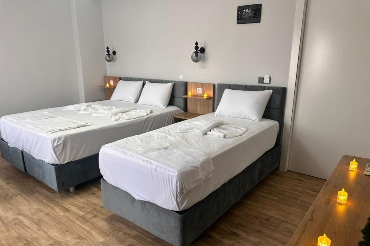 A hotel room with two beds, a wooden floor, and a nightstand with candles.