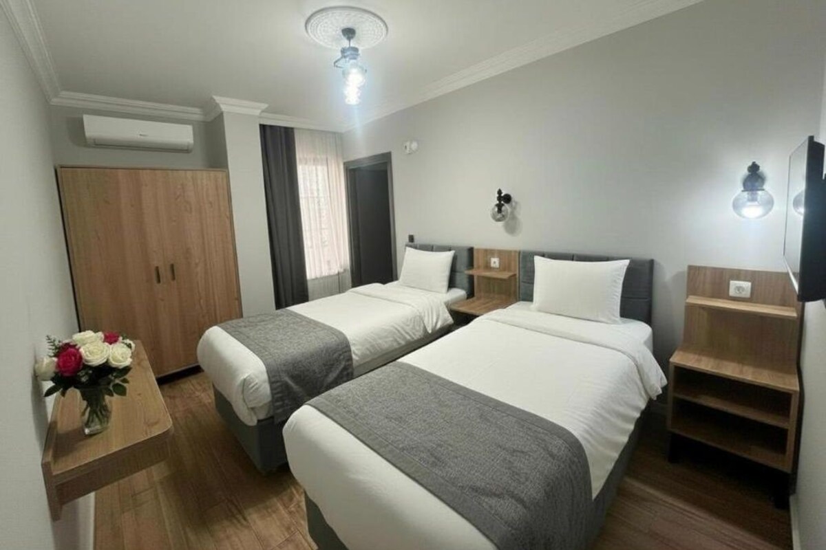 A hotel room with two beds, a wooden wardrobe, a small table with a vase of flowers, and a ceiling fan.